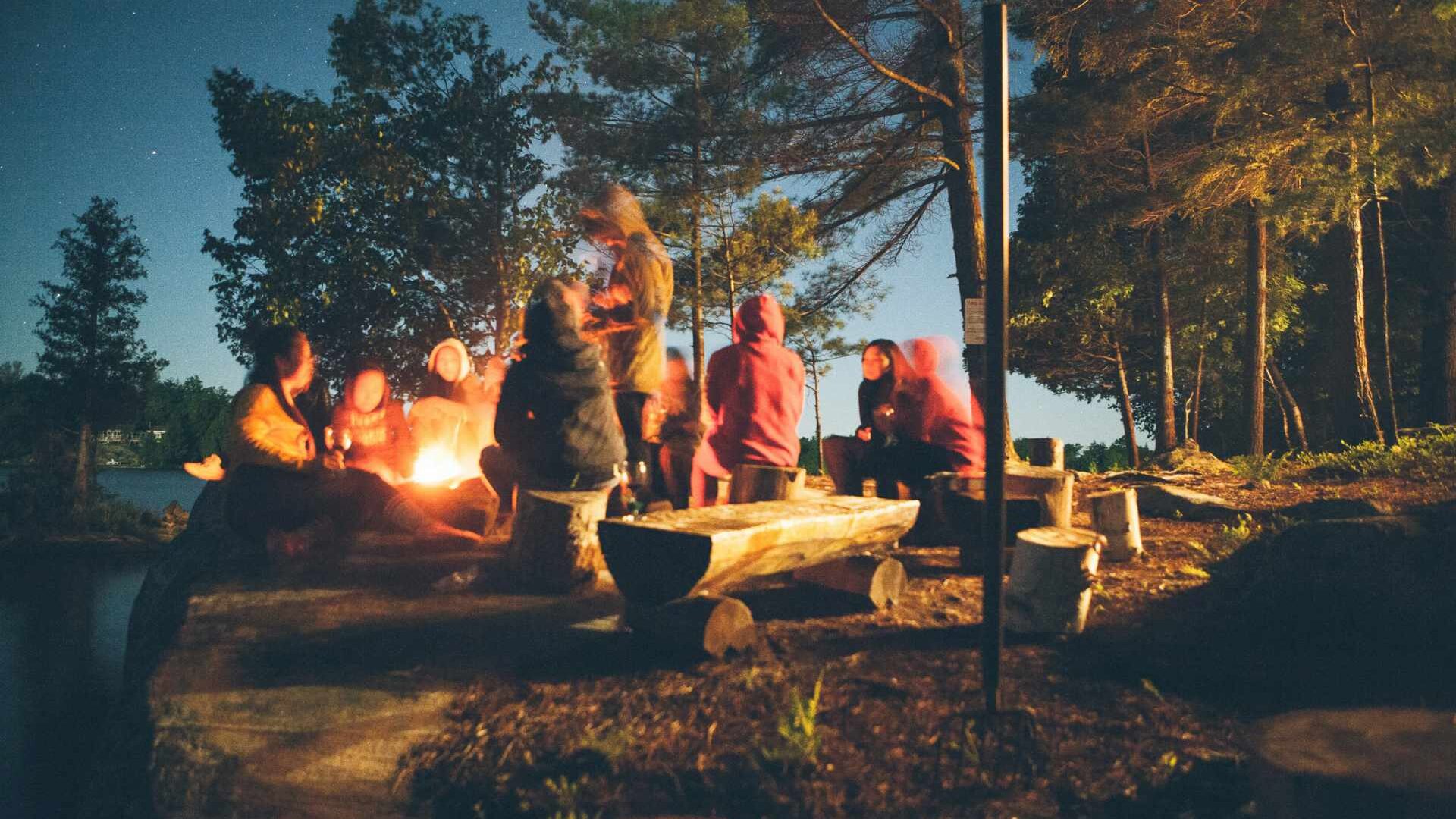 Teenage children sitting at dusk around a campfire on Summer Camp