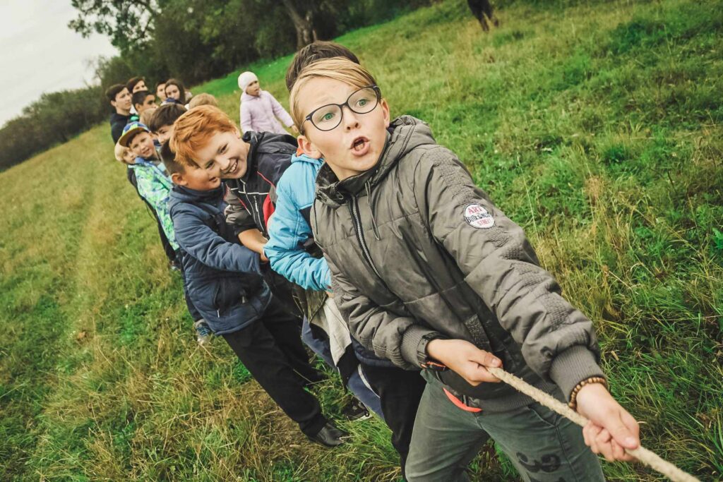 Kids at Summer School playing tug of war in a grassy field